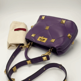 Valentino Garavani Roman Stud pequena em couro nappa roxo com ferragens douradas.
